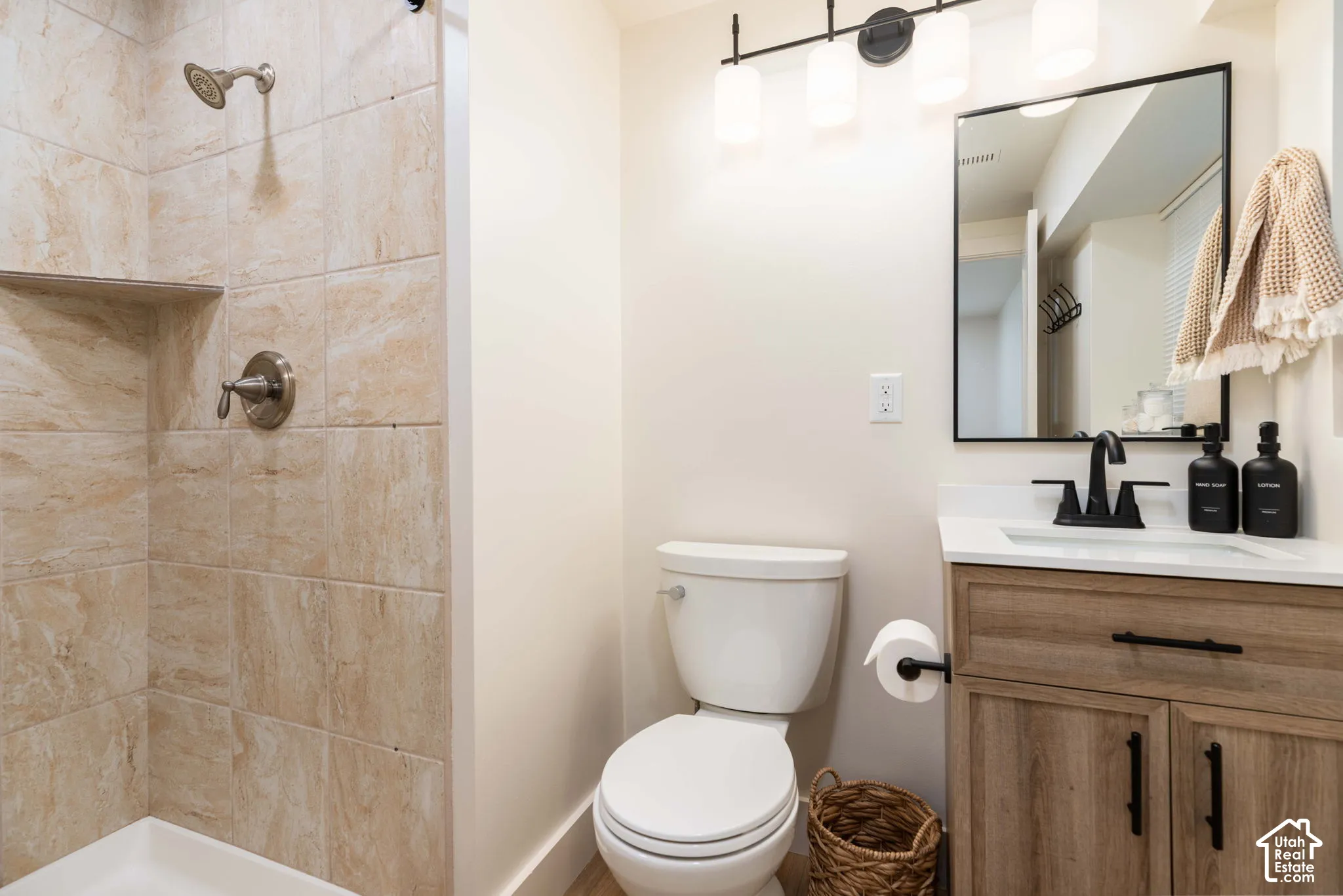 Bathroom featuring a walk-in shower with tiled walls and a built-in shelf, a toilet, and a vanity with wood-finish cabinetry, a white countertop, and a black-framed mirror