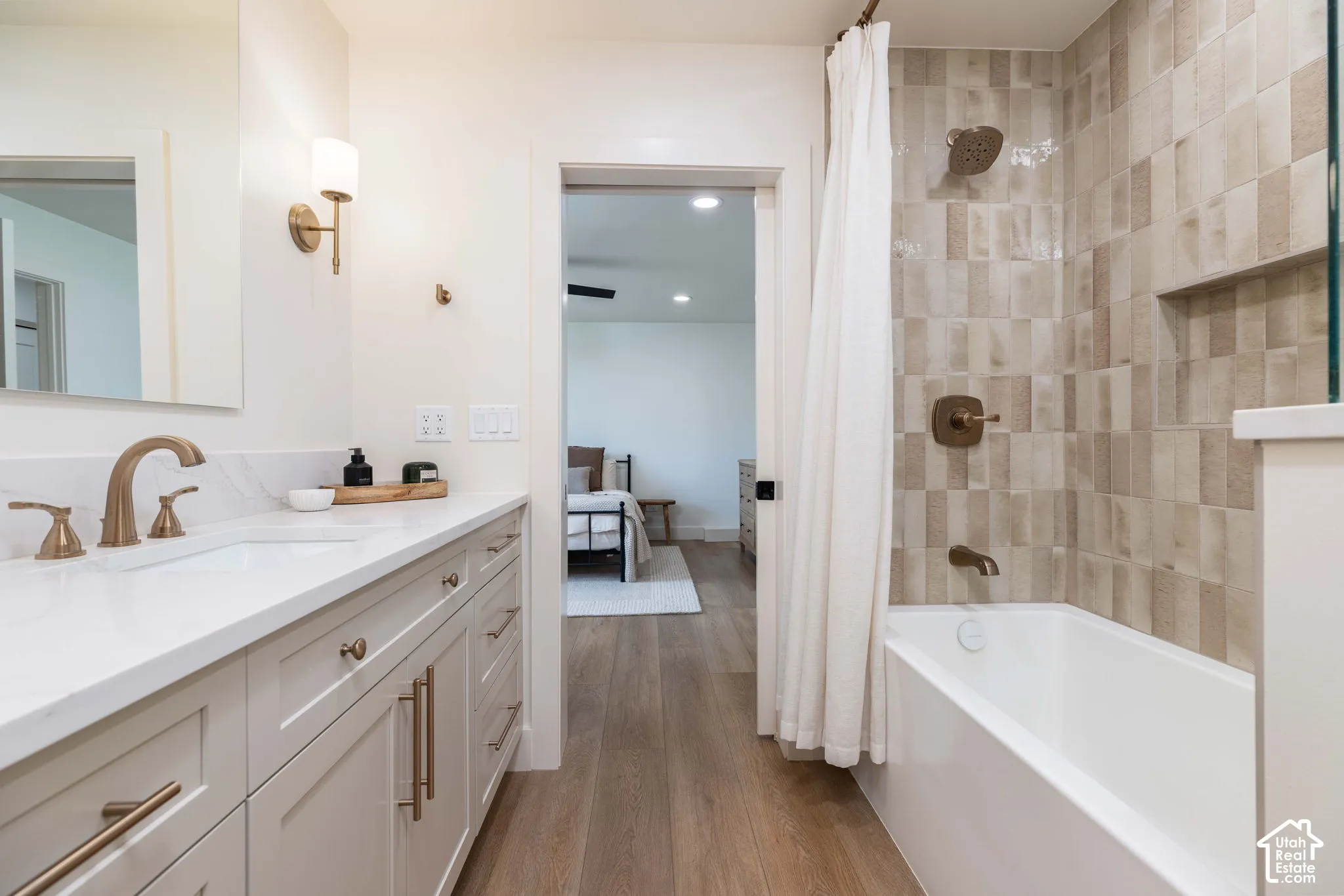 Bathroom featuring a long single vanity with a white countertop and undermount sink, brushed gold fixtures, and light-toned cabinetry