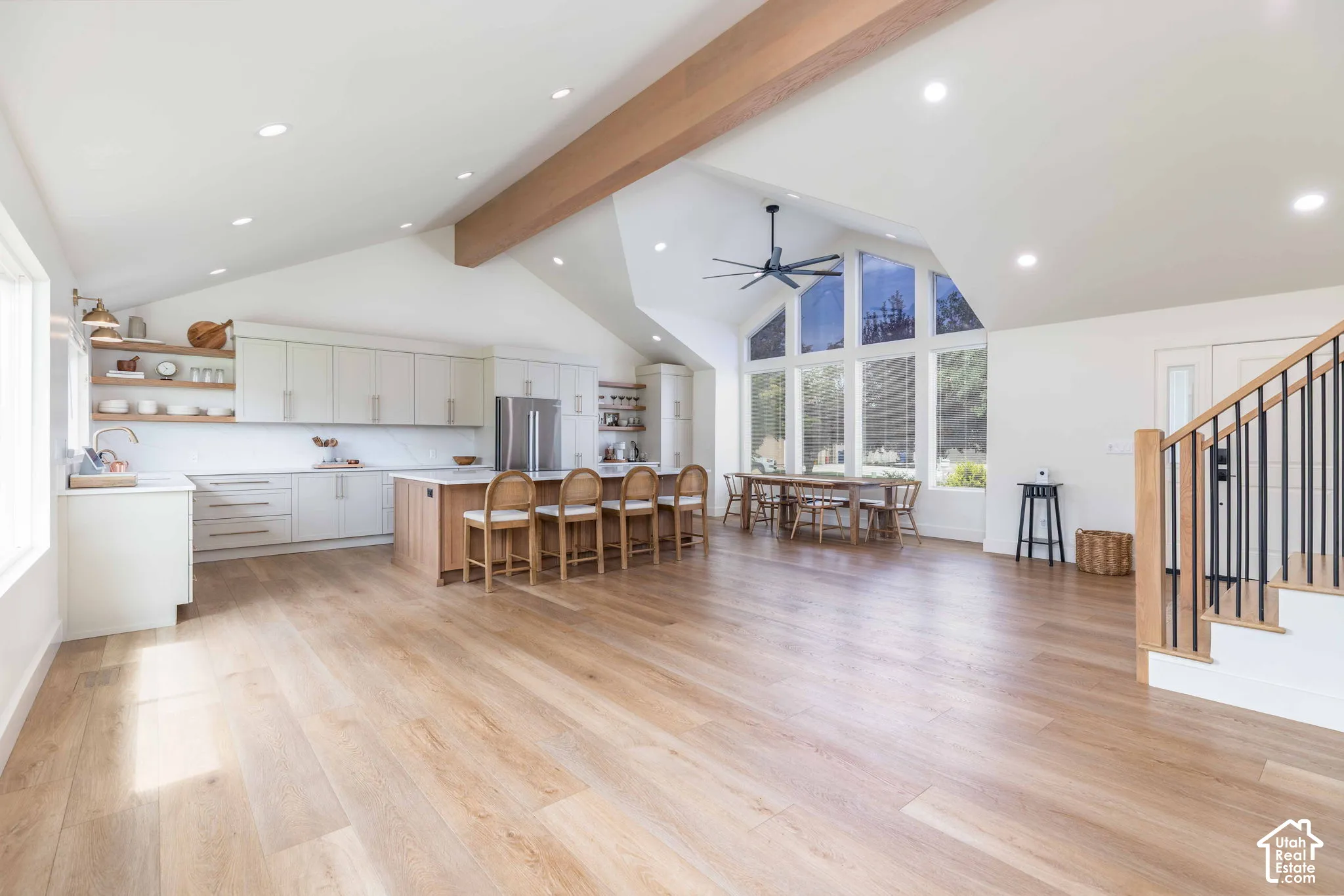 Spacious open-concept living area featuring wood-finish flooring, a vaulted ceiling with a visible beam, and recessed lighting