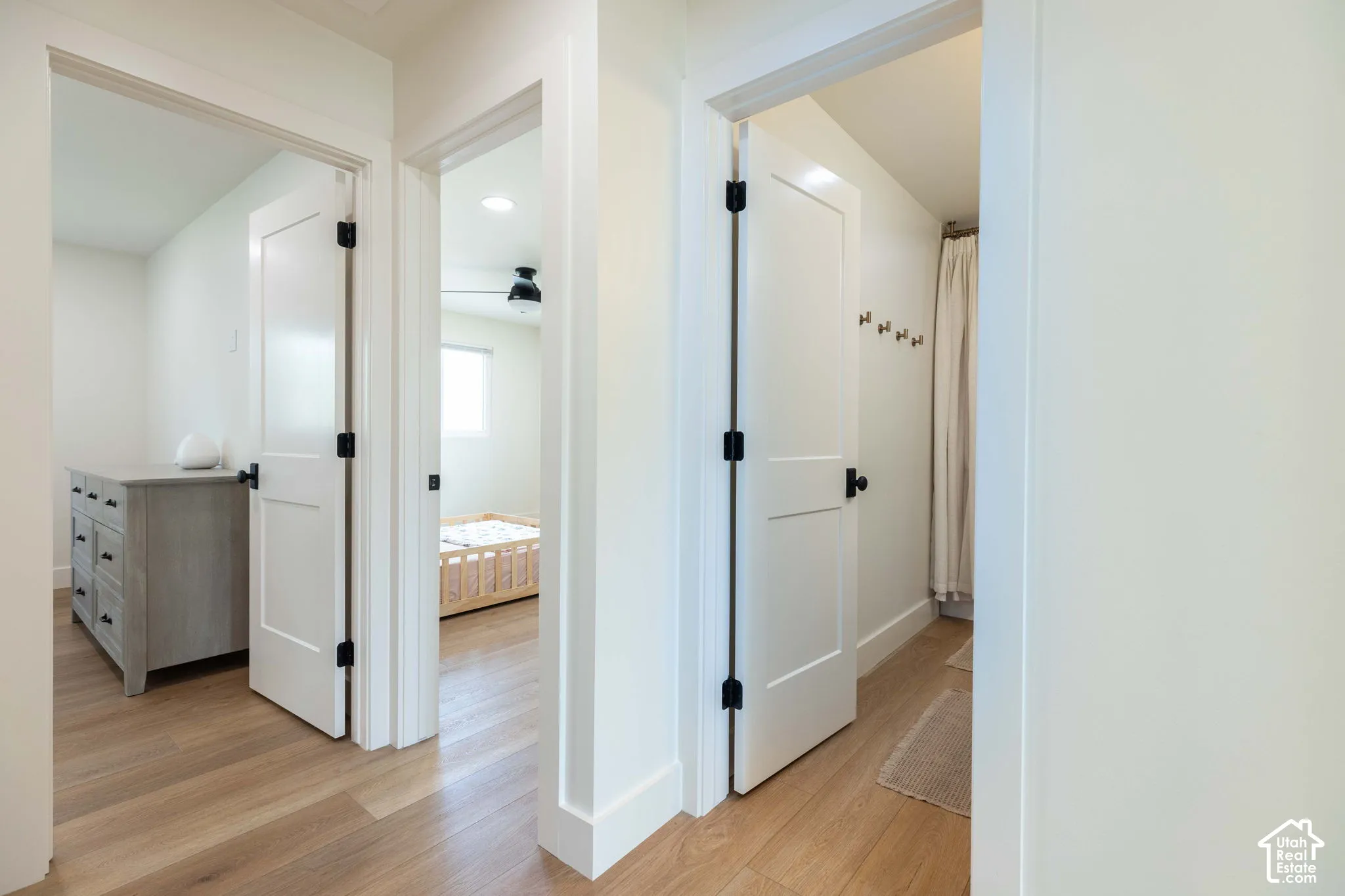 Hallway featuring wood-finish flooring, white paneled doors with matte black hardware, and crisp white baseboards