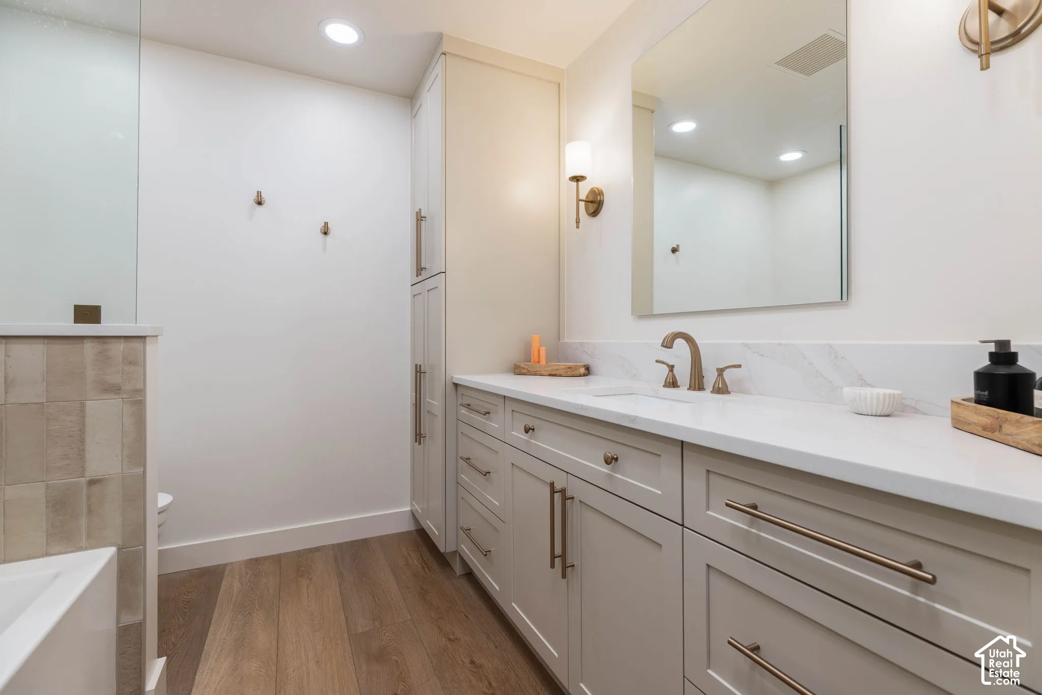 Spacious bathroom featuring a double vanity with stone countertops, integrated sink, and modern cabinetry with brushed bronze hardware