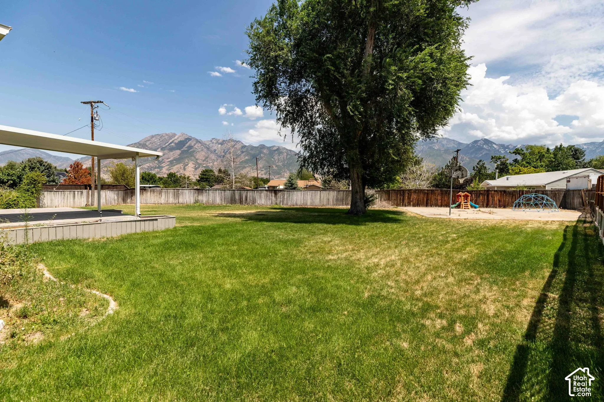 Expansive backyard featuring a large tree, a covered patio, and a wood fence enclosing the perimeter