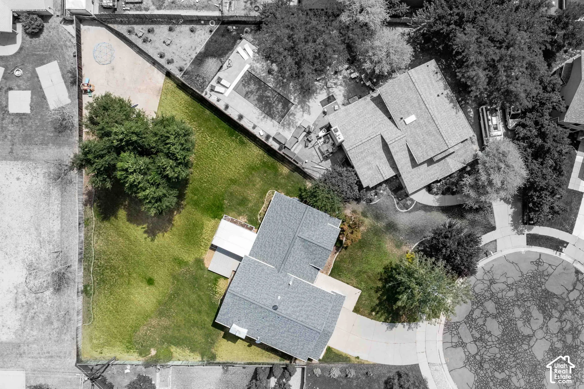Expansive green lawn surrounds the property, featuring mature trees and a paved driveway leading to the residence