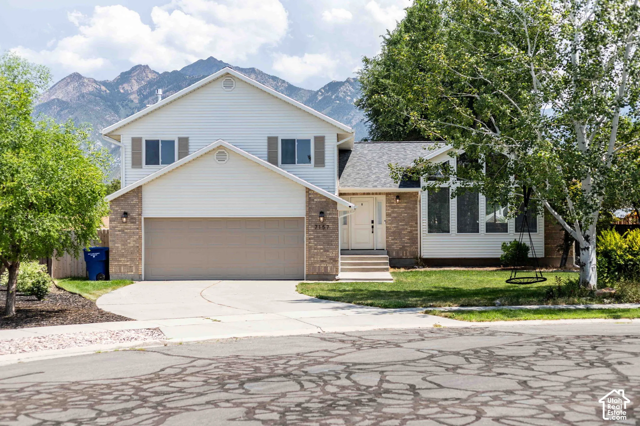 Two-story traditional residence with mountain backdrop, featuring a two-car garage, brick and siding exterior, established front landscaping, and a pitched roof