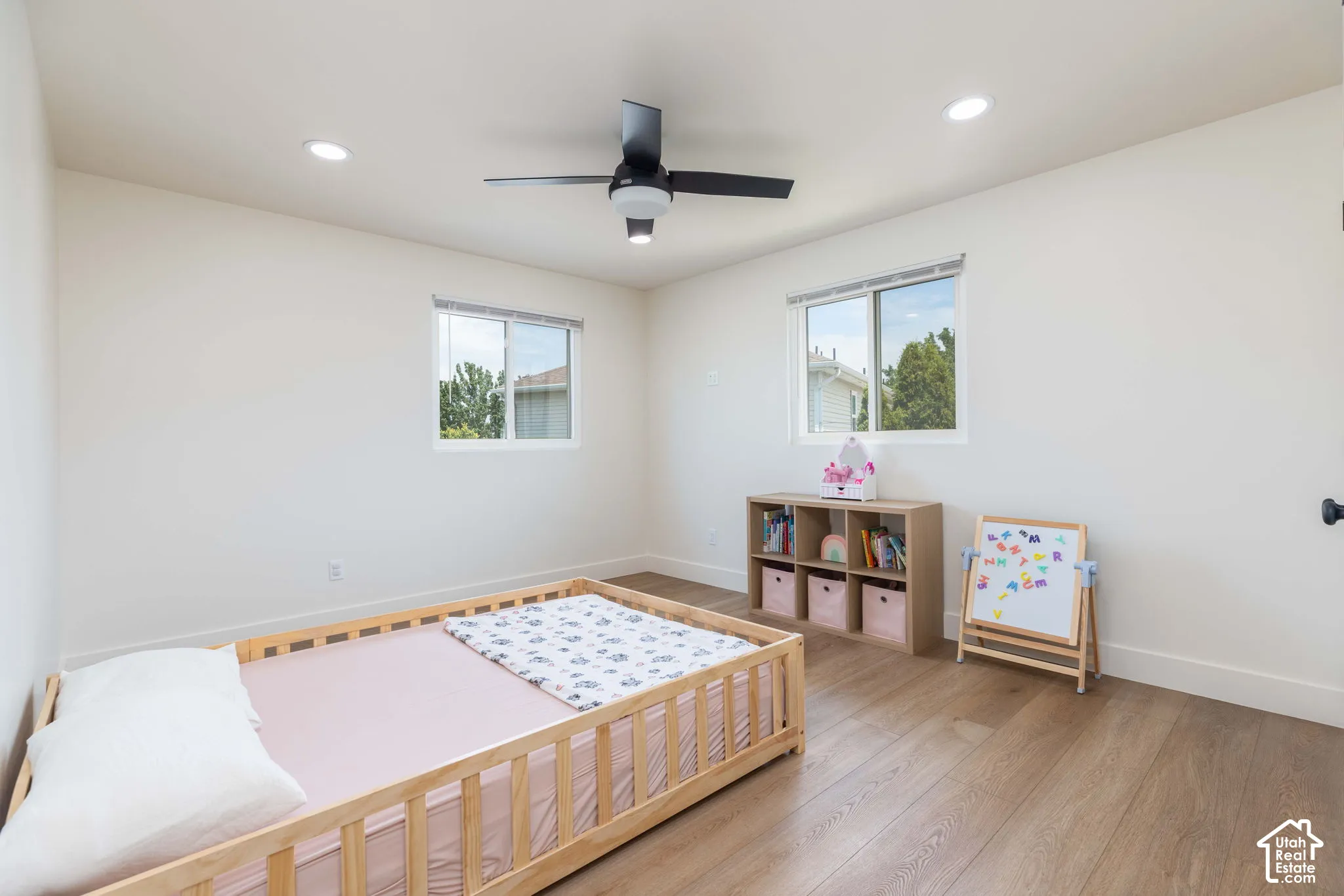 Spacious room featuring wood-finish flooring, white walls, and a black ceiling fan with integrated lighting