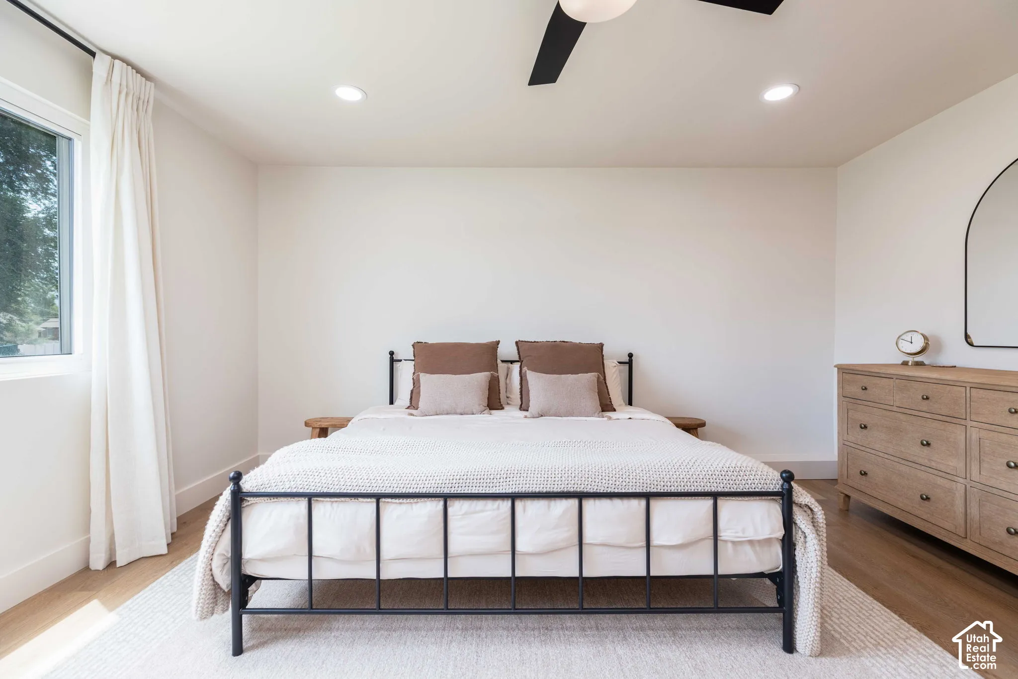 Recessed lighting illuminates this room featuring wood-finish flooring, a contemporary ceiling fan, and a large window with roller shades
