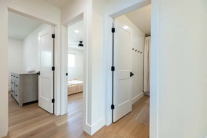 Hallway featuring wood-finish flooring, white paneled doors with matte black hardware, and crisp white baseboards