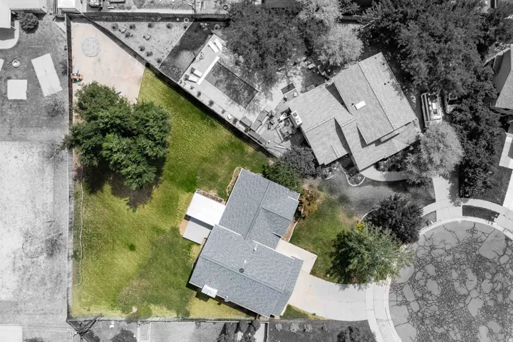 Expansive green lawn surrounds the property, featuring mature trees and a paved driveway leading to the residence