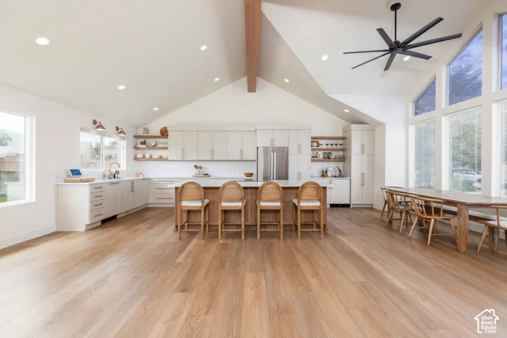 Open-concept living space featuring vaulted ceilings with exposed wood beams, wood-finish flooring, a kitchen island with seating, a full suite of stainless steel appliances, and expansive windows