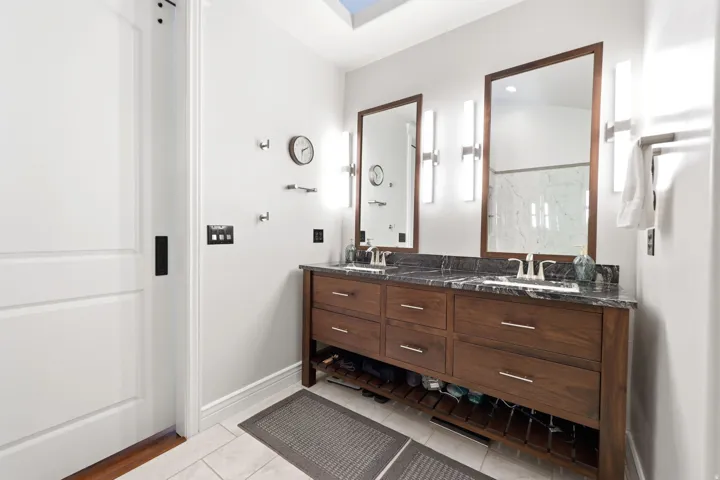 Double vanity featuring wood cabinetry, a dark stone countertop, undermount sinks, and individual framed mirrors