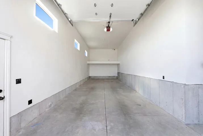Spacious garage featuring a concrete floor, high ceilings, multiple transom windows, and a built-in storage shelf
