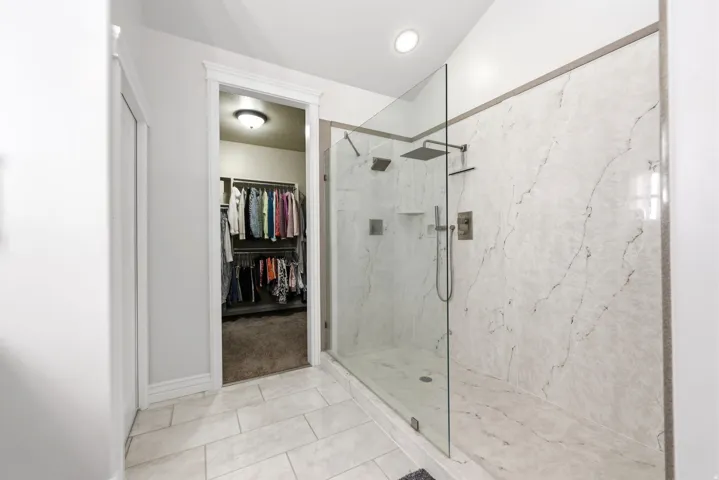Spacious walk-in shower featuring large format veined wall tiles, a frameless glass enclosure, and multiple showerheads