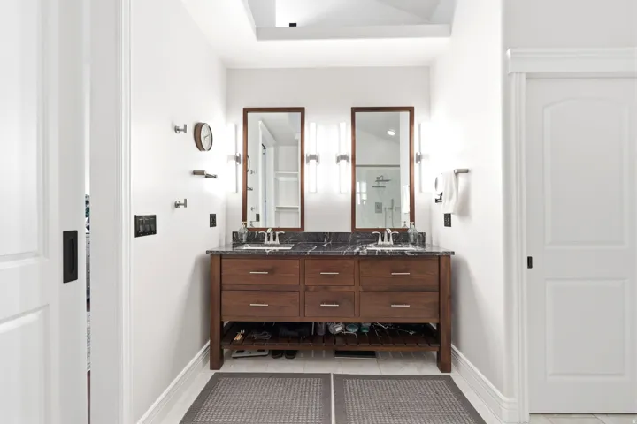 Dual vanity with rich wood-finish cabinetry and a dark stone countertop featuring integrated sinks