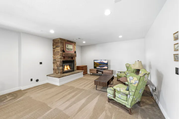 Stone-stacked fireplace with a raised hearth, wood mantle, recessed lighting, and neutral carpeting