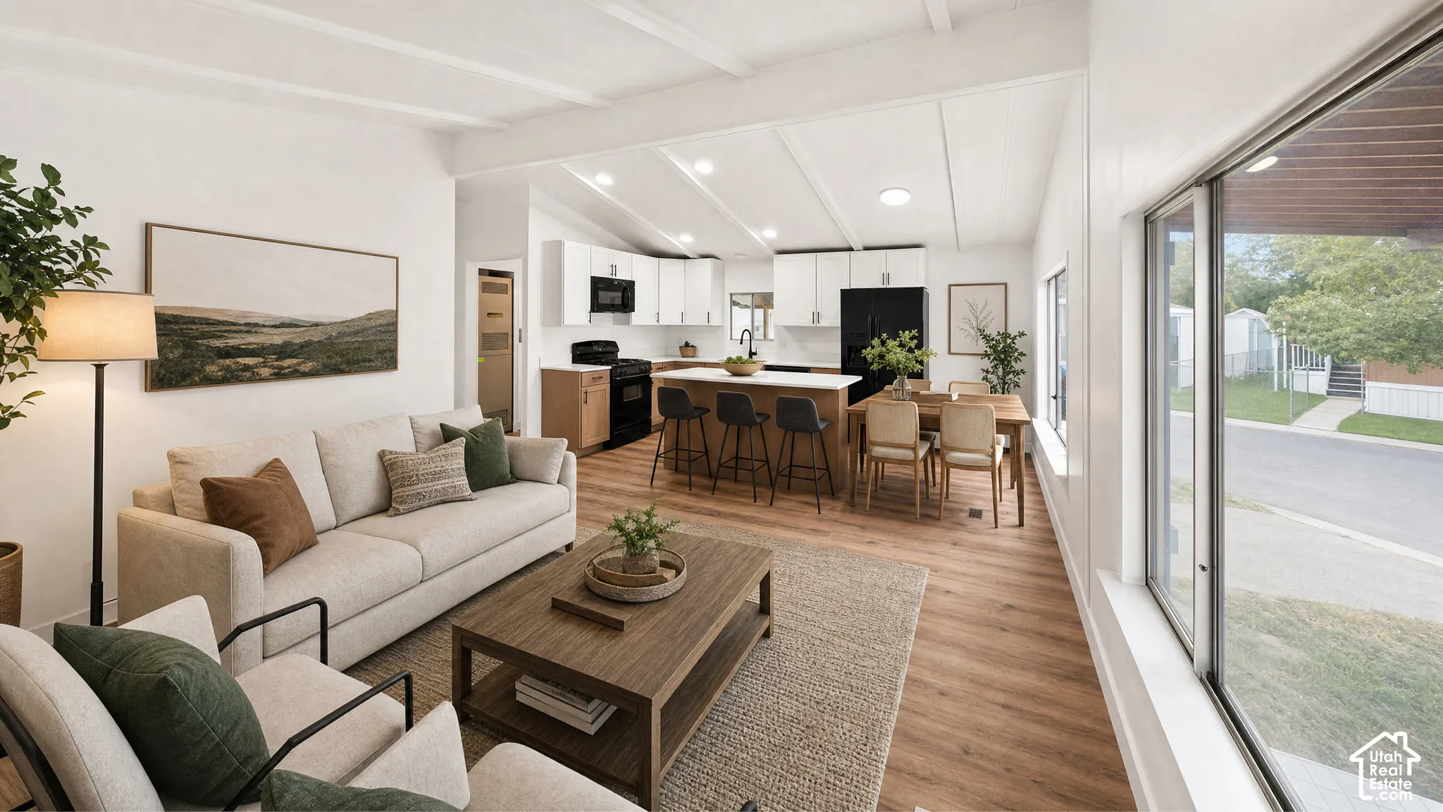 Open-concept living space featuring wood-finish flooring, vaulted ceilings, and large windows