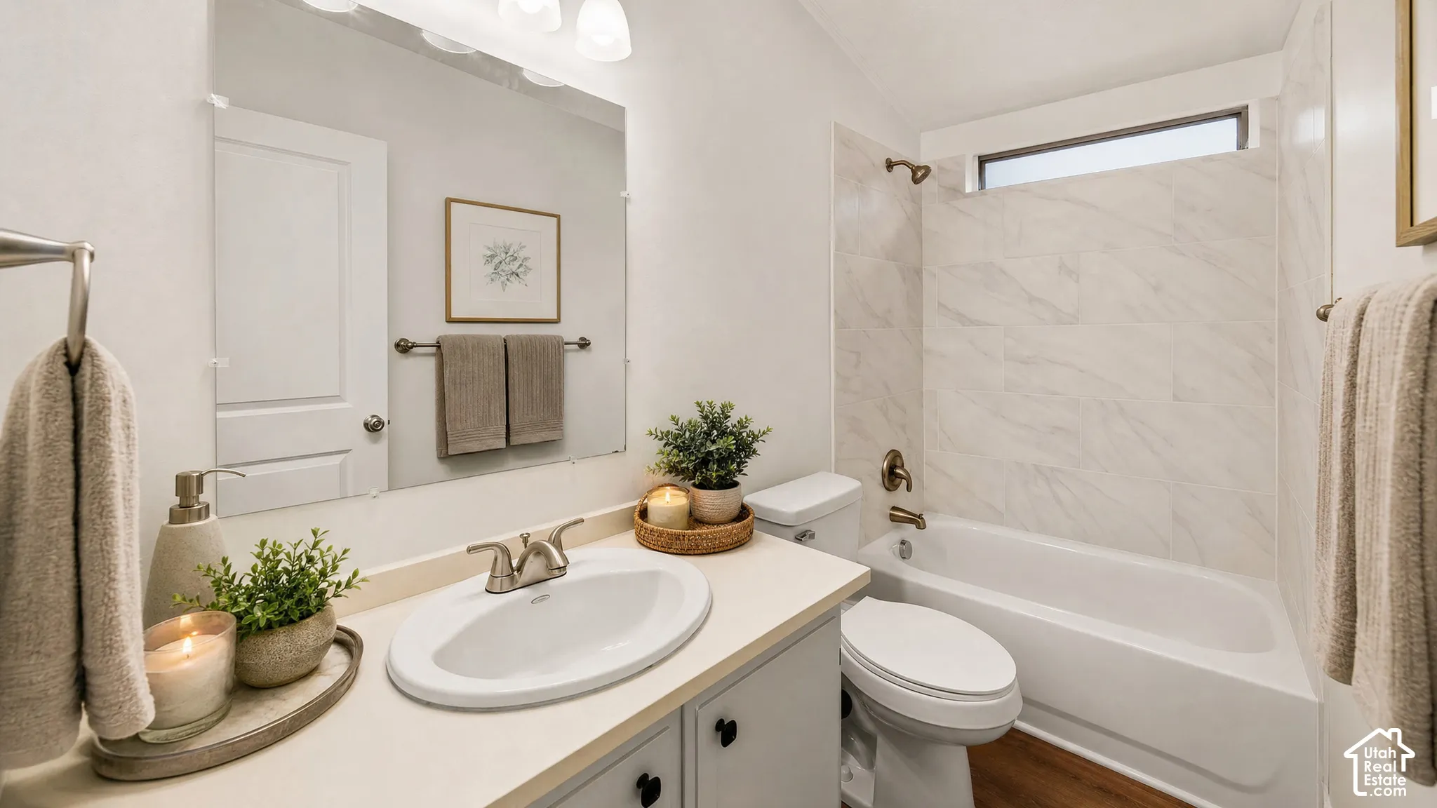 Bathroom featuring a light-toned vanity with an integrated sink, a large wall-mounted mirror, brushed nickel fixtures, a tub with a tiled surround, and wood-finish flooring