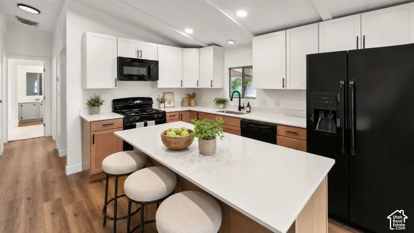 Modern kitchen featuring a central island with a light-toned countertop, two-tone cabinetry with white upper and wood-finish lower units, and black appliances