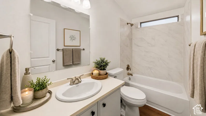 Bathroom featuring a light-toned vanity with an integrated sink, a large wall-mounted mirror, brushed nickel fixtures, a tub with a tiled surround, and wood-finish flooring