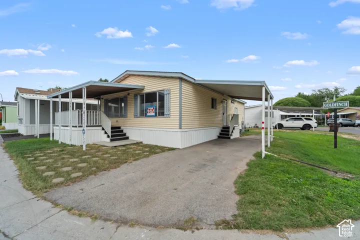 Single-story residence featuring light-colored siding, a covered front porch with railings, and an additional covered carport