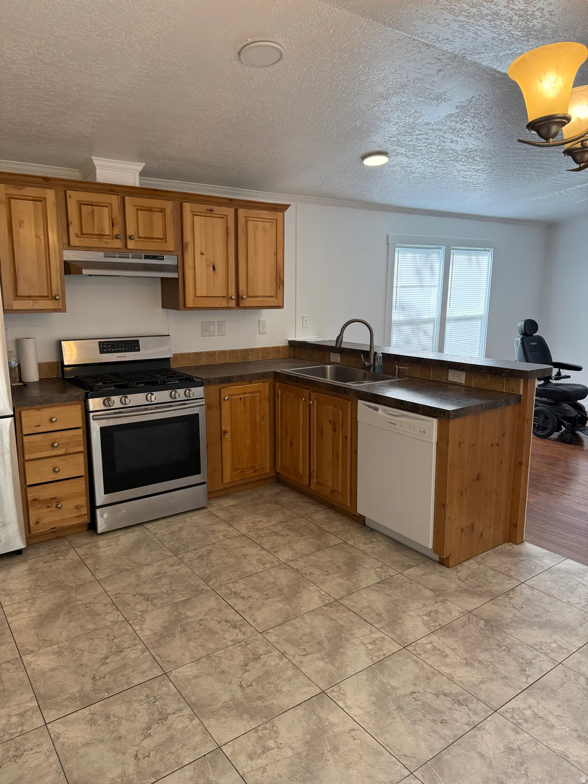 Kitchen featuring light wood cabinetry with crown molding, stainless steel gas range, stainless steel sink with gooseneck faucet, white dishwasher, and tile flooring