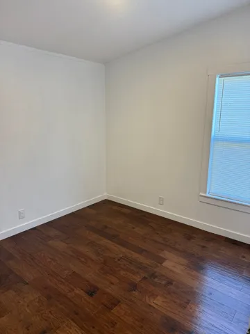 Interior room featuring wood-finish flooring, white baseboards, and a window with horizontal blinds