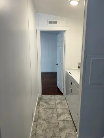 Hallway with gray-toned square tile flooring leading to an interior room featuring dark wood-finish flooring