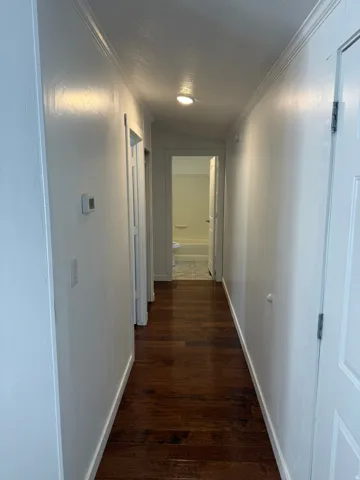 Hallway featuring wood-finish flooring, white painted walls, and crown molding