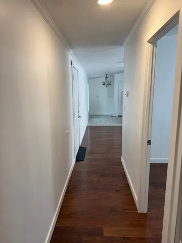 Hallway with wood-finish flooring, white walls, and crown molding