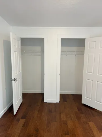 Dual closets featuring paneled doors, wire shelving, and wood-finish flooring
