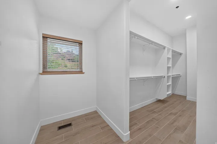 Spacious walk-in closet featuring wood-finish flooring, white walls, and a window with wood blinds