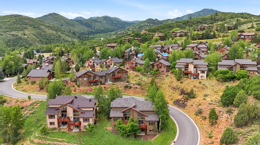 Mountain community featuring multiple multi-story residences with diverse architectural styles, mature trees, and paved roads