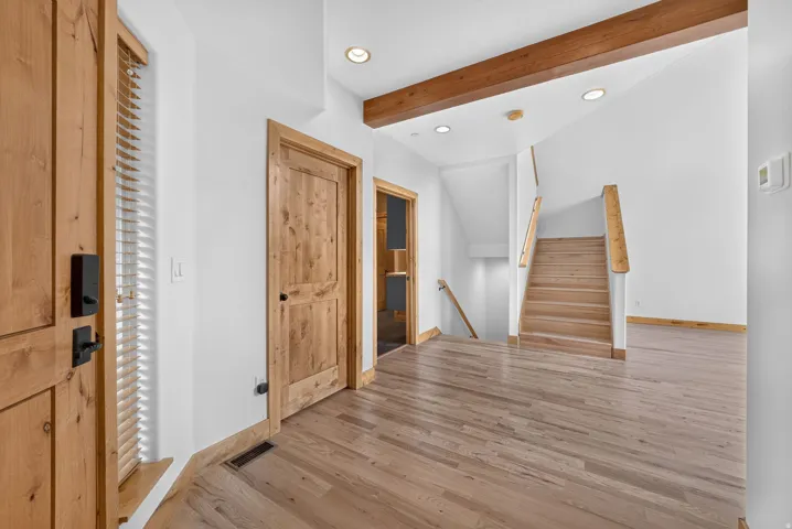 Entryway with wood-finish flooring, a solid wood door with black hardware, and a staircase featuring wood treads and railings
