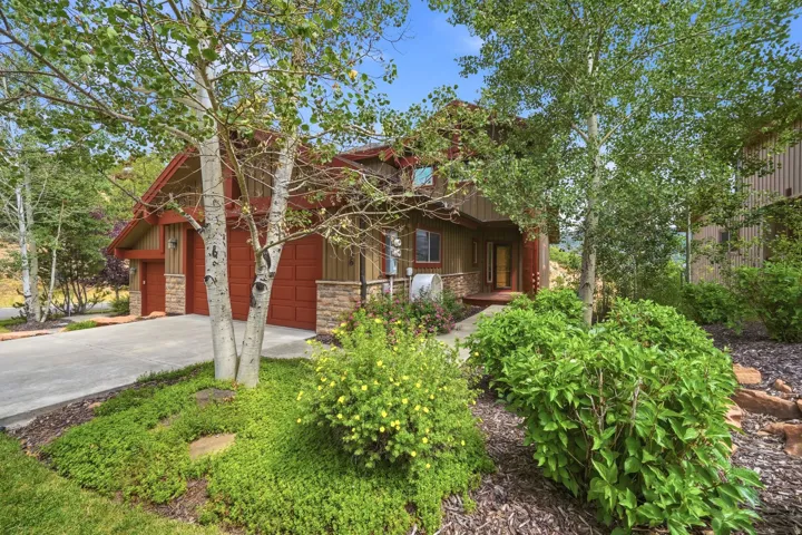 Rustic-style exterior featuring a multi-toned facade, attached two-car garage, mature landscaping, and a concrete driveway