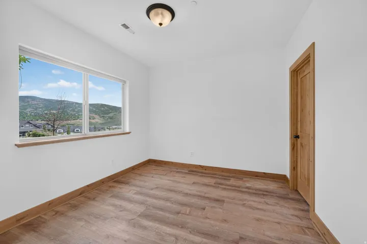 Room featuring a large picture window, wood-finish flooring, white walls, wood trim, and a wood panel door