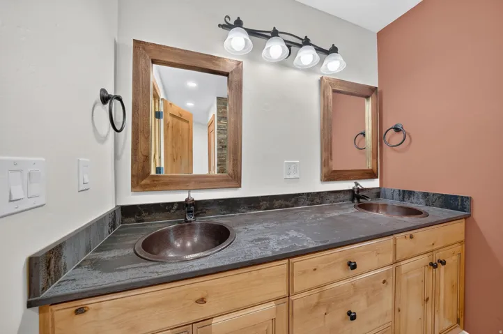 Dual copper vessel sinks with bronze-finish faucets set into a dark countertop with matching backsplash