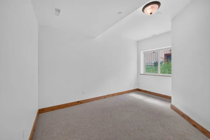 Carpeted room featuring a white window frame, wood-finish base trim, and a ceiling-mounted light fixture