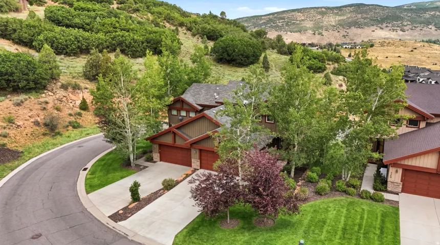 Mountain-style residence featuring a two-car garage with wood-finish doors, a concrete driveway, and a manicured lawn