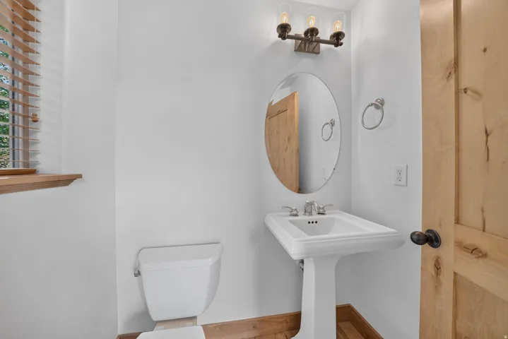 Pedestal sink with chrome faucet, oval mirror, and wall-mounted vanity lighting