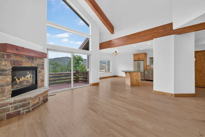 Open-concept living space featuring a stone-faced fireplace with a wood mantel, wood-finish flooring, and vaulted ceilings with exposed wood beams