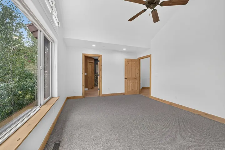 Spacious room featuring vaulted ceilings, a large window, a ceiling fan, and carpeted flooring