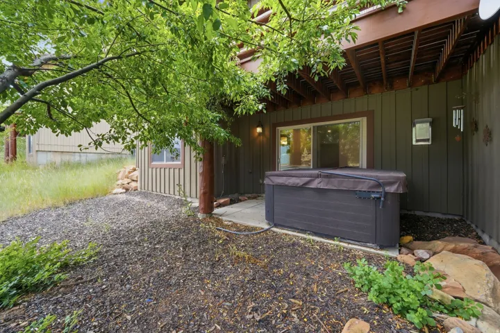 Outdoor spa situated on a concrete patio beneath a wooden deck, featuring a sliding glass door entry to the interior