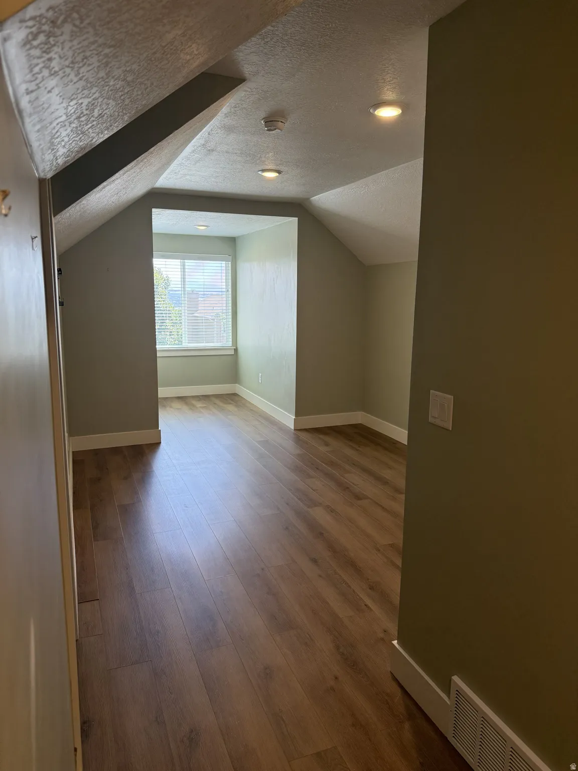 Attic room featuring wood-finish flooring, recessed lighting, and a window with horizontal blinds