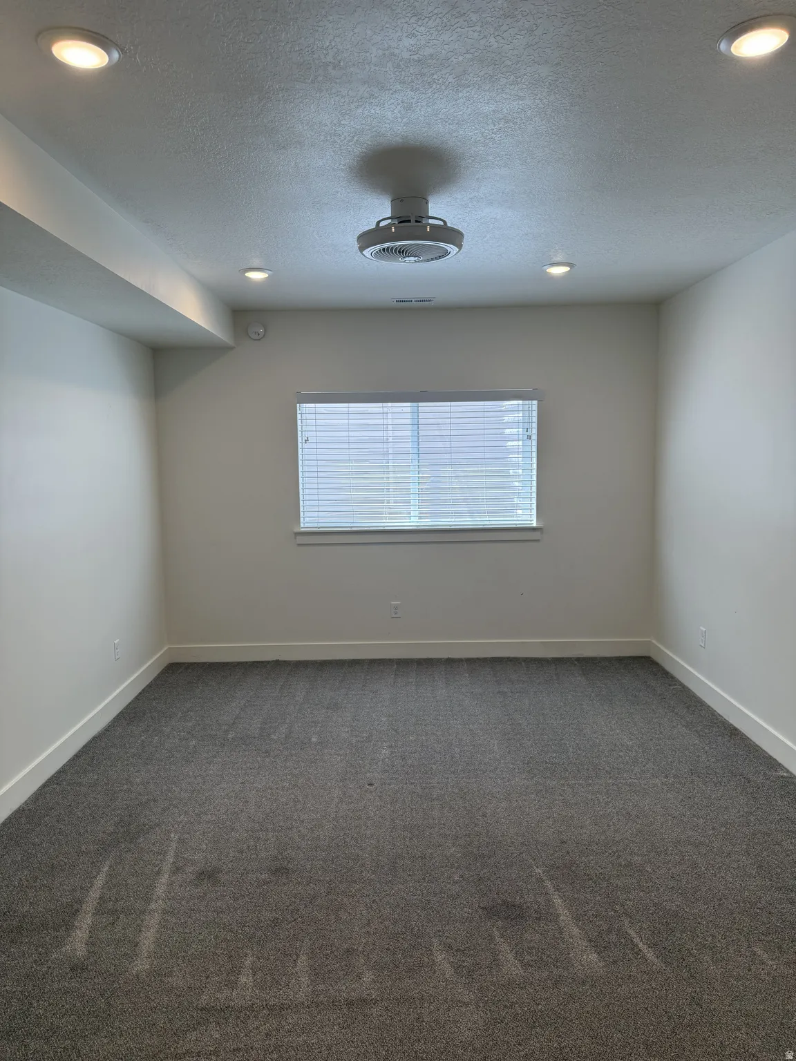 Spacious room featuring gray carpeting, white walls, and bright recessed lighting