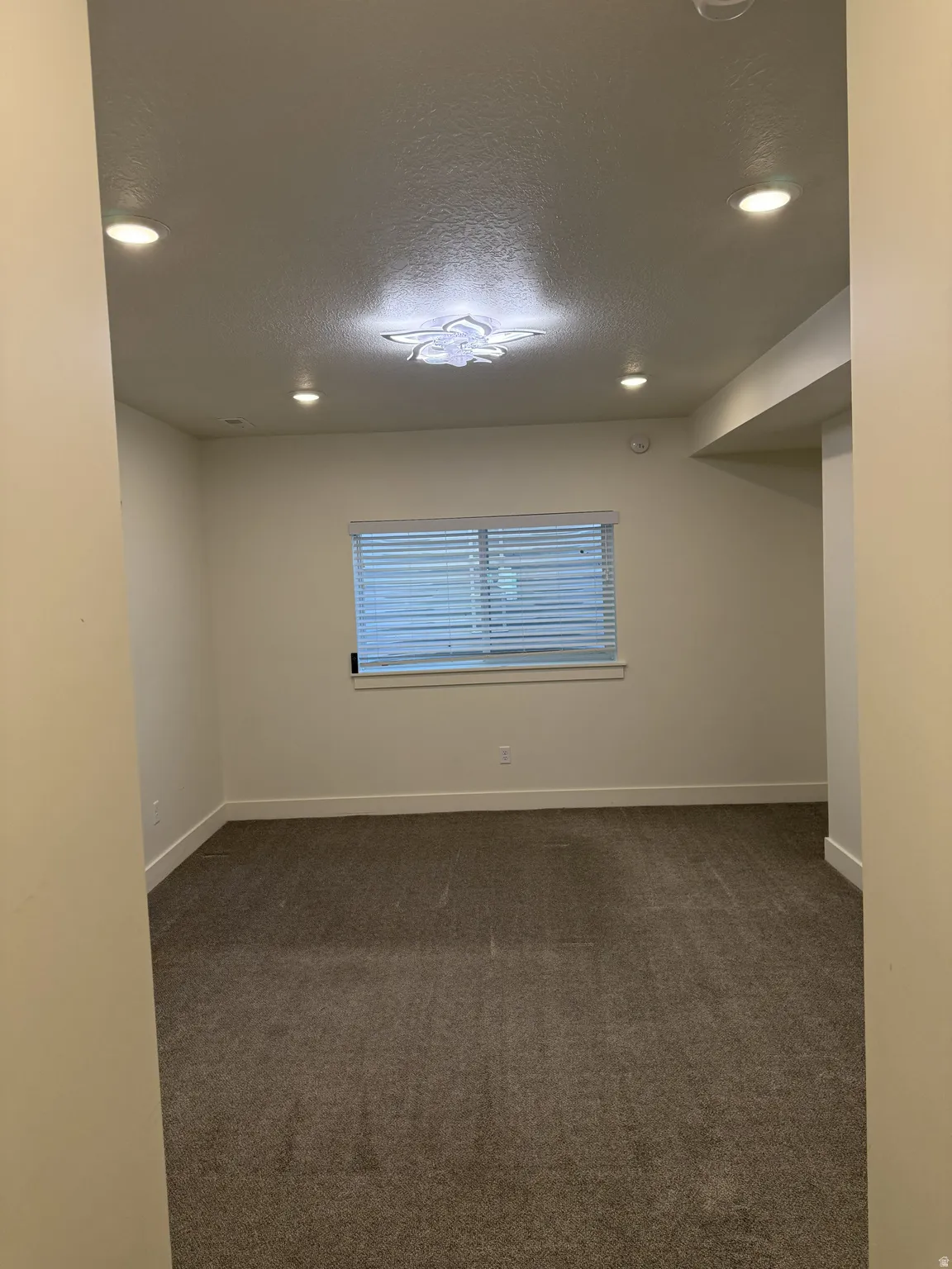 Carpeted room featuring a window with horizontal blinds, recessed ceiling lighting, and a decorative flush-mount ceiling fixture