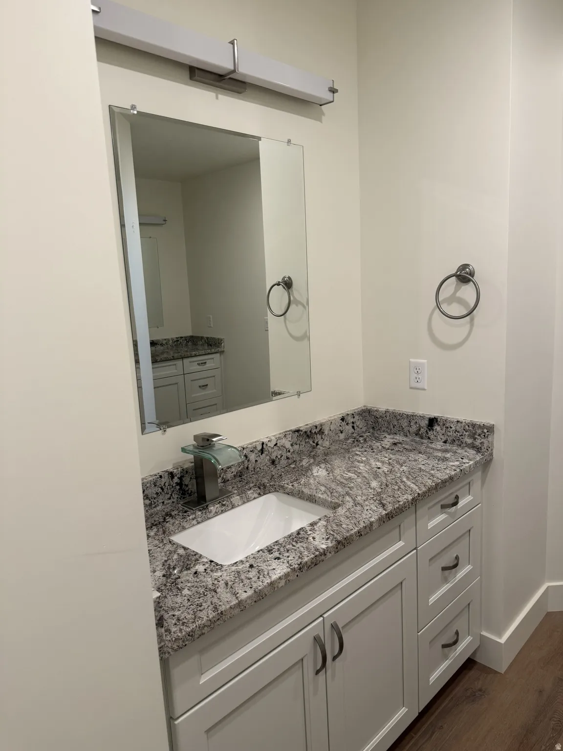 Vanity with speckled countertop, undermount sink, and light wood-finish flooring