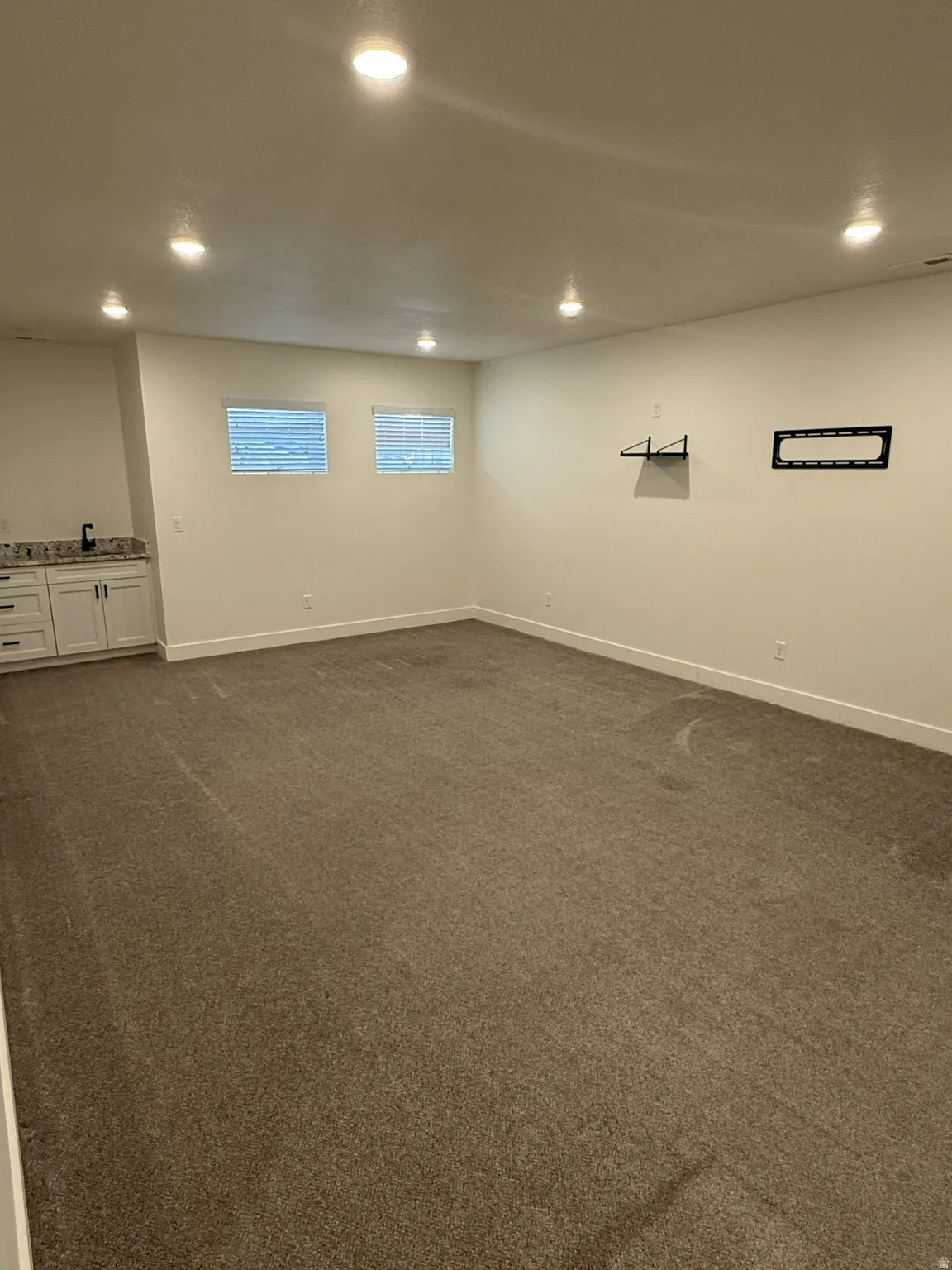 Spacious room featuring neutral carpeting, recessed ceiling lighting, and a built-in wet bar with white cabinetry, a dark countertop, and a black faucet