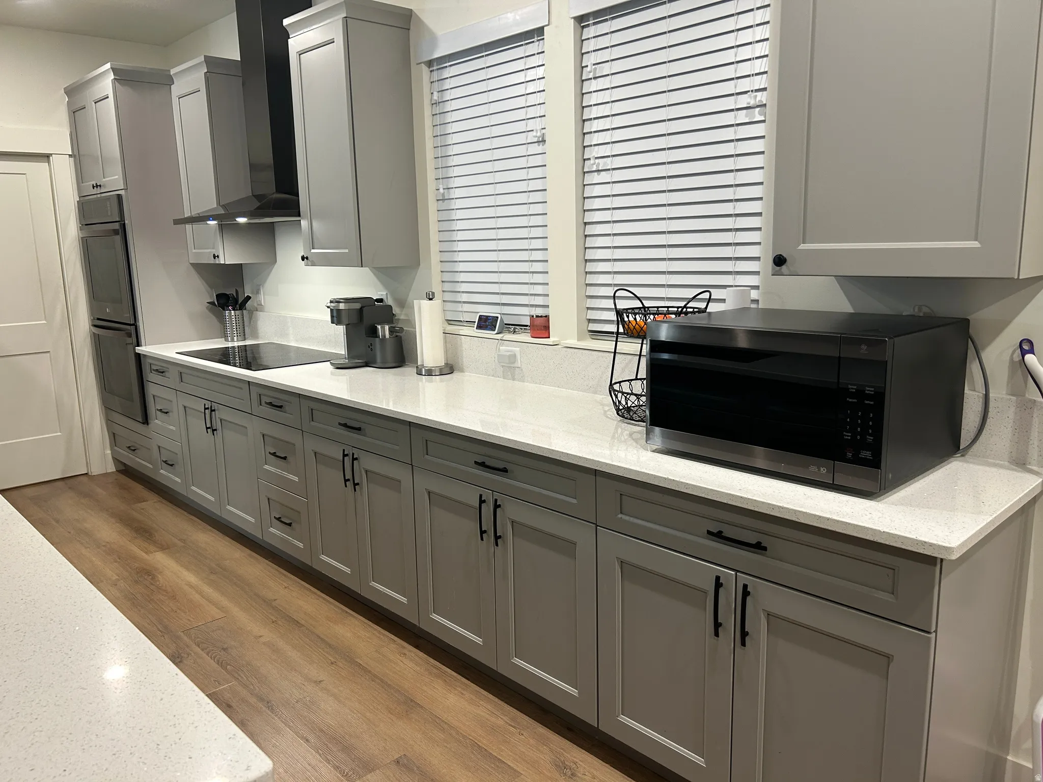 Contemporary kitchen featuring extensive gray shaker-style cabinetry, light-toned countertops, and wood-finish flooring