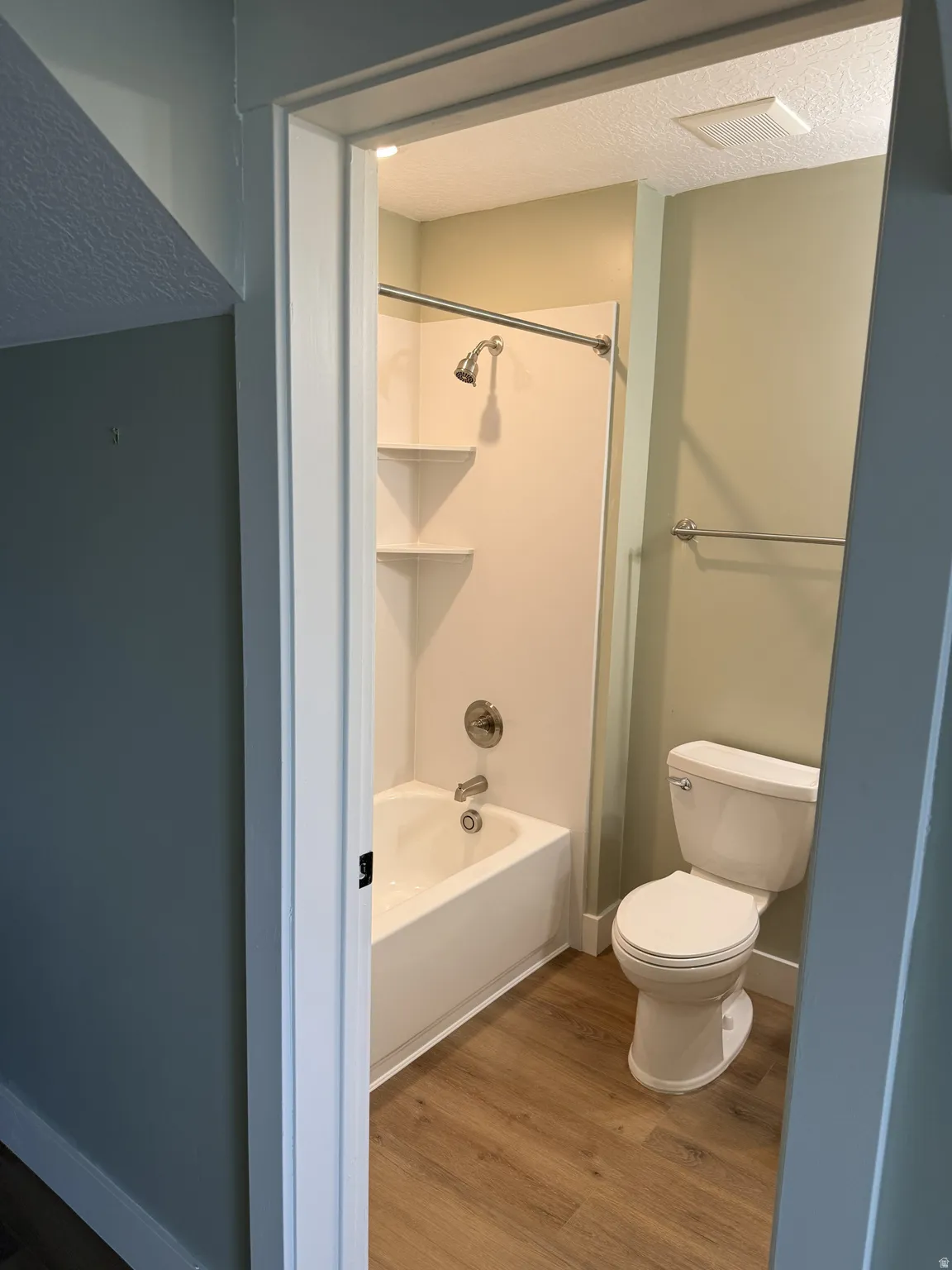 Bathroom featuring a white tub and shower combination with an integrated shelving unit, brushed nickel fixtures, and wood-finish flooring