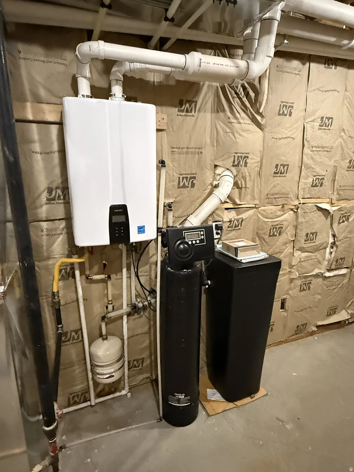 Tankless water heater installation featuring PVC piping and insulation-backed wall