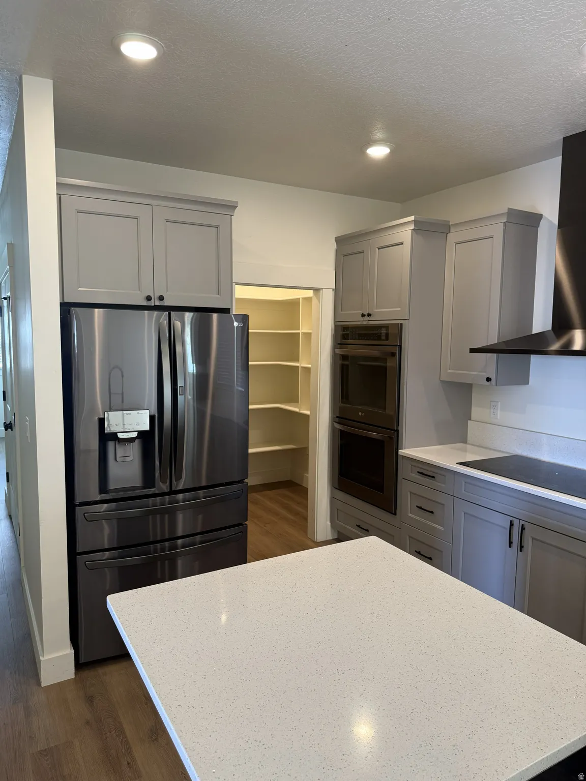 Contemporary kitchen featuring a white quartz-finish island countertop, stainless steel refrigerator, built-in double oven, sleek cooktop, and a walk-in pantry with ample shelving